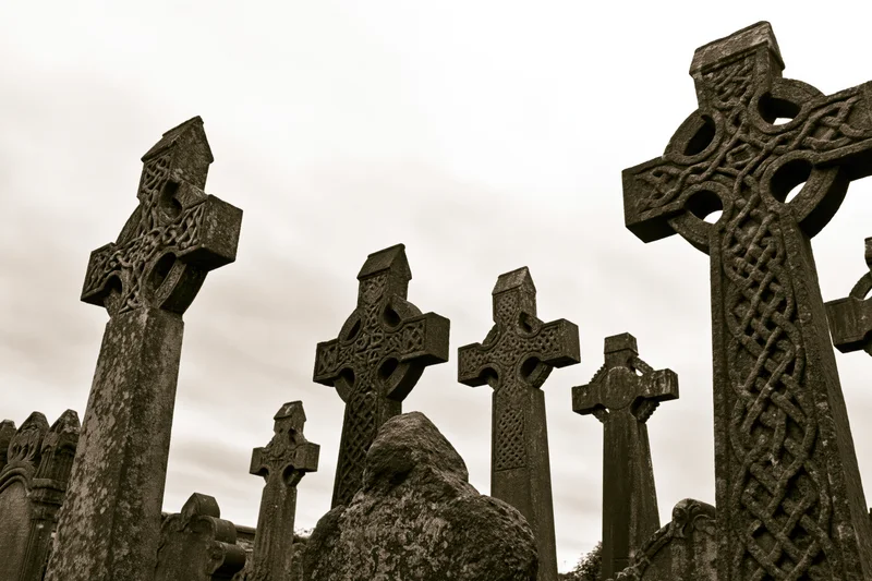 Weathered celtic stone crosses standing in a cemetery under an overcast sky