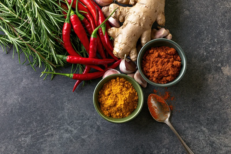Fresh and dried cooking ingredients arranged along the left edge of a dark stone surface with copyspace on the right