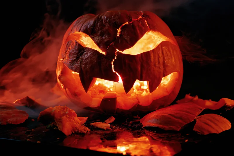 Cracked jack-o-lantern glowing with smoke and broken pieces around it on dark surface