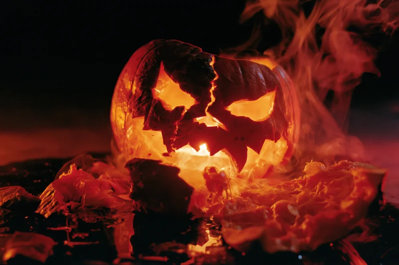 Cracked jack-o-lantern glowing with smoke rising from broken pieces on dark ground