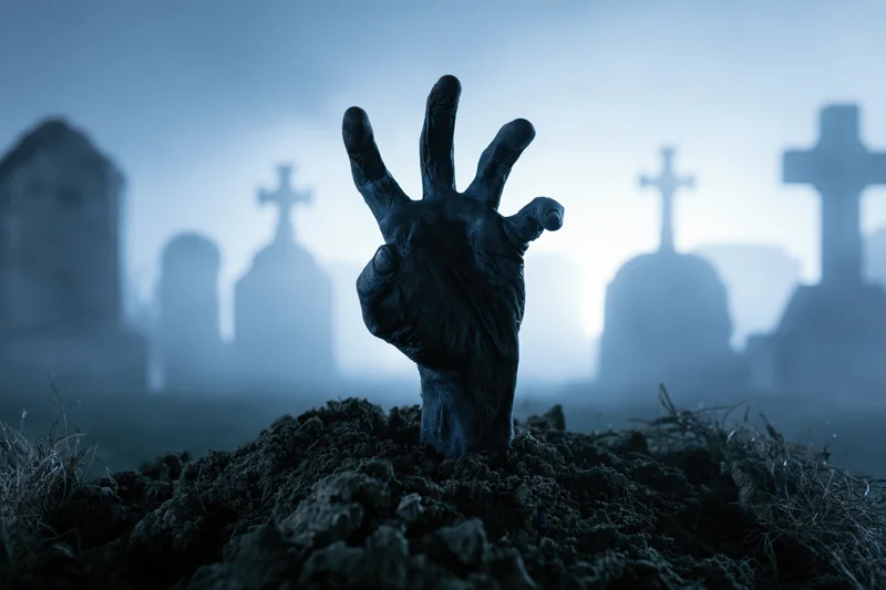 Zombie hand emerging from dirt in a foggy graveyard with tombstones in the background