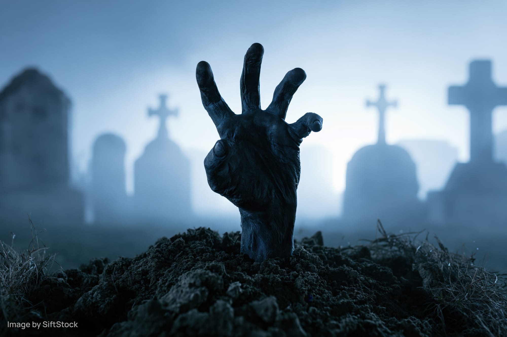 Zombie hand emerging from dirt in a foggy graveyard with tombstones in the background