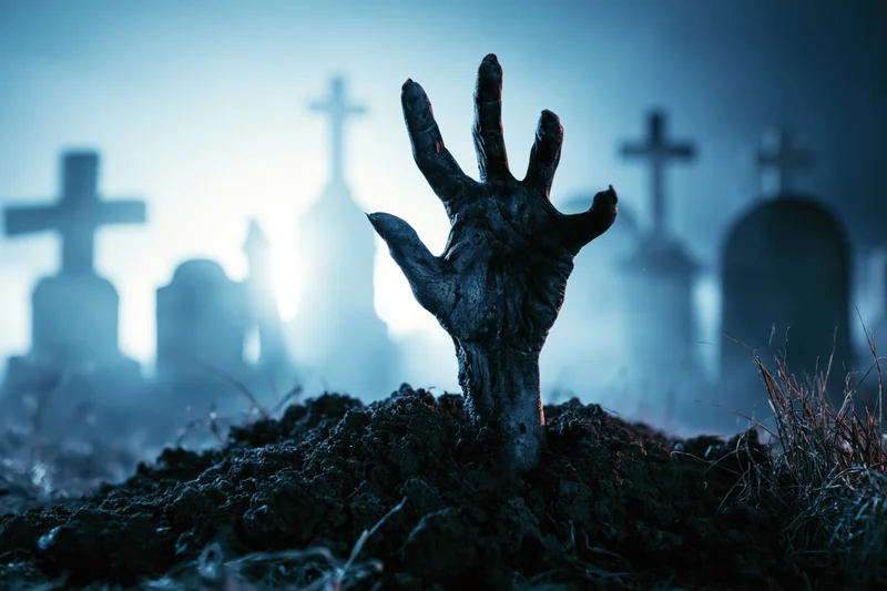 Decayed zombie hand emerging from dirt in a foggy graveyard at night