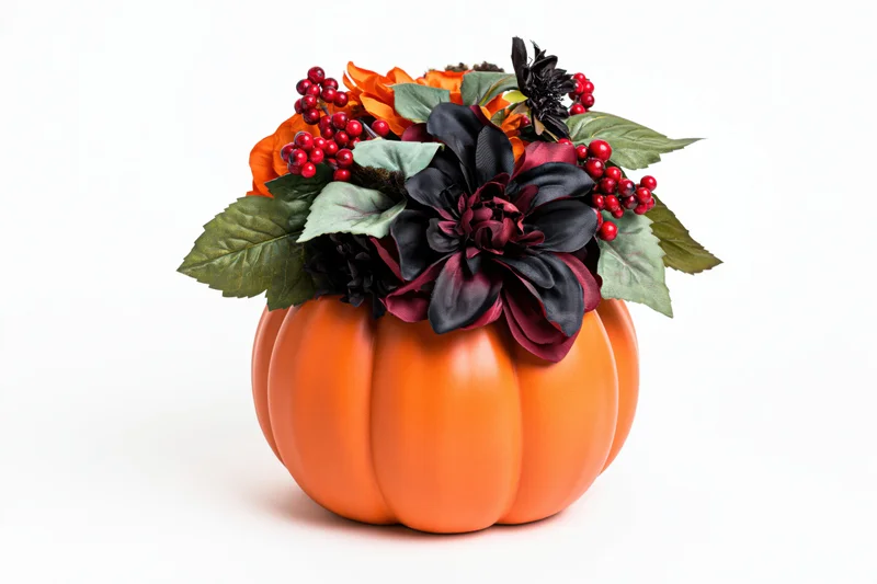 Ceramic pumpkin centerpiece topped with artificial flowers and berries on white background
