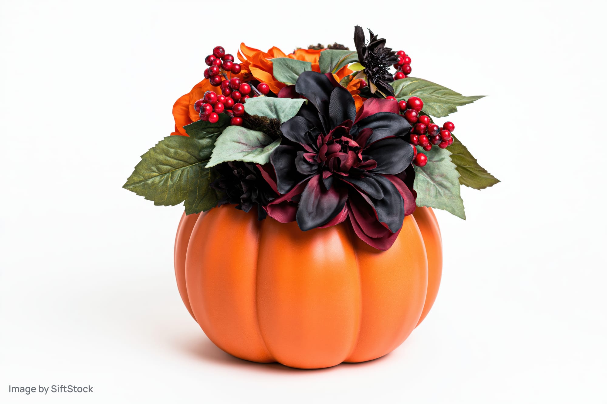 Ceramic pumpkin centerpiece topped with artificial flowers and berries on white background