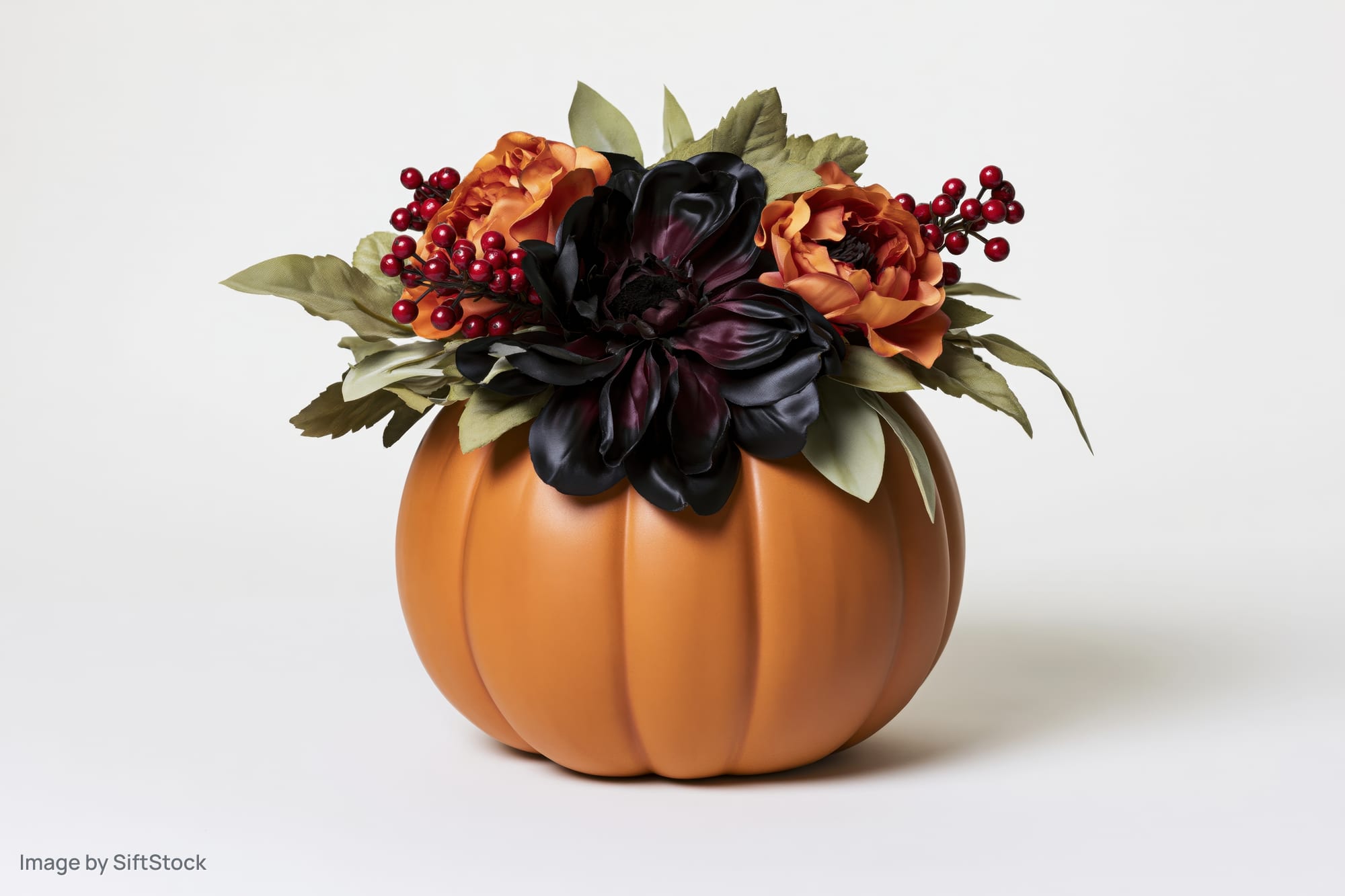 Ceramic pumpkin centerpiece topped with artificial flowers and berries on white background