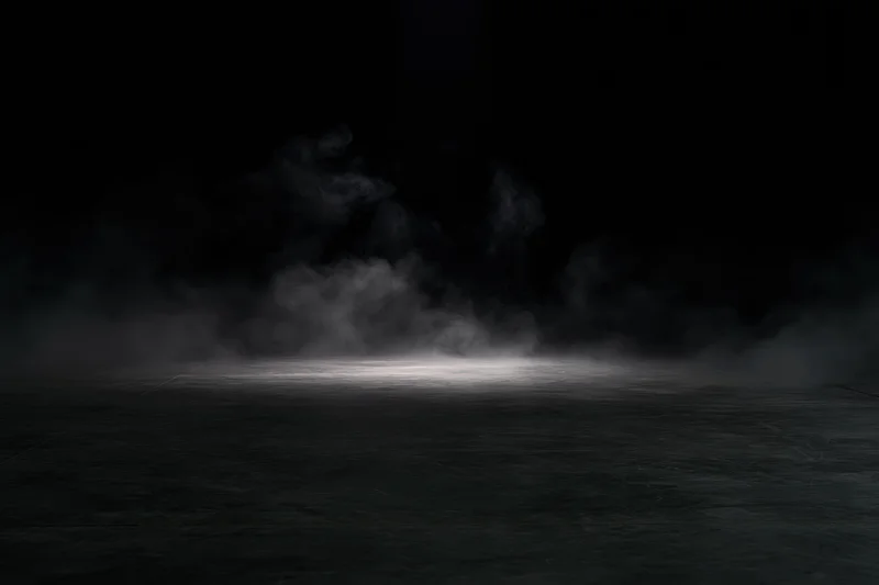 Smoke rising from a dark concrete floor under a spotlight