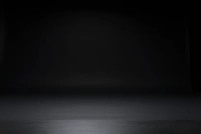 Empty dark studio backdrop with seamless black surface and subtle lighting gradient