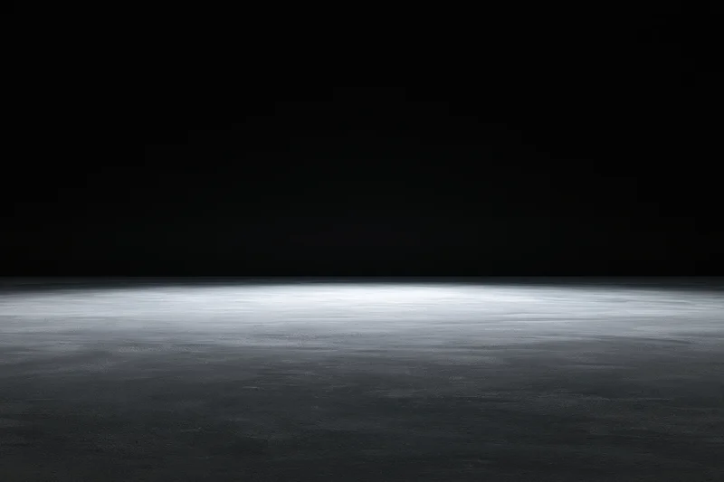 Dark studio interior with spotlighted concrete floor and black backdrop