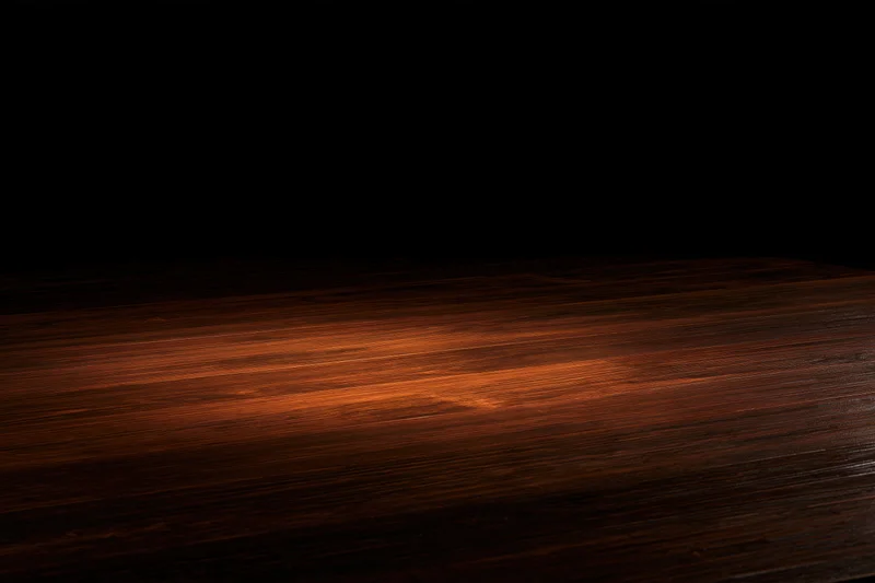 Dark wooden surface illuminated by a narrow spotlight against black background