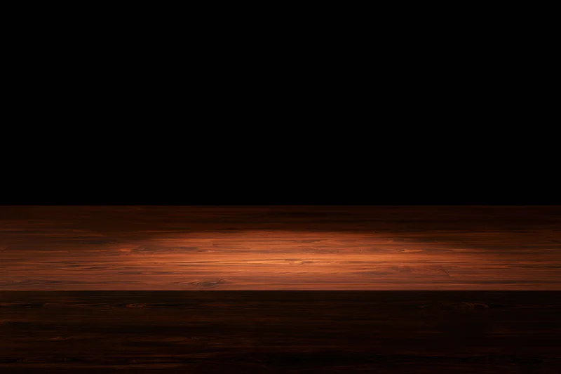 Dark wooden surface illuminated by a single spotlight with warm glow and shadowed edges
