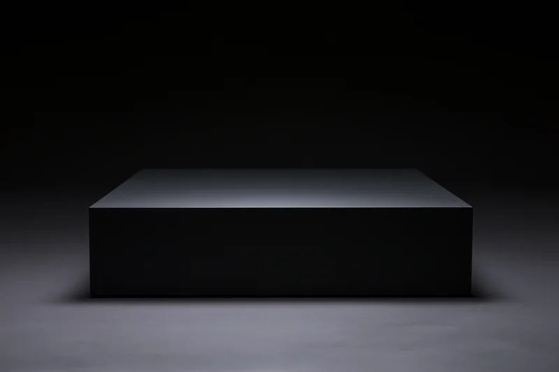 Matte black rectangular pedestal on a dark floor under spotlight lighting