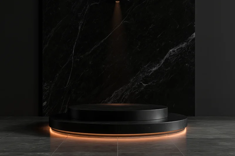 Two-tiered black stone pedestal with warm lighting in a dark showroom space