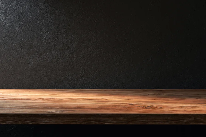 Empty wooden tabletop against dark textured plaster wall with copyspace for product display