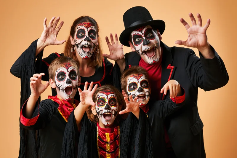 Family in halloween skeleton costumes posing with raised hands in studio