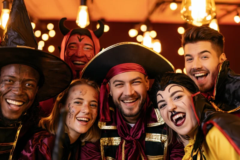Five adults in halloween costumes posing together indoors smiling at camera