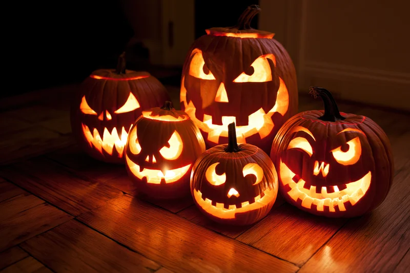 Five carved jack-o-lanterns glowing on a wooden floor