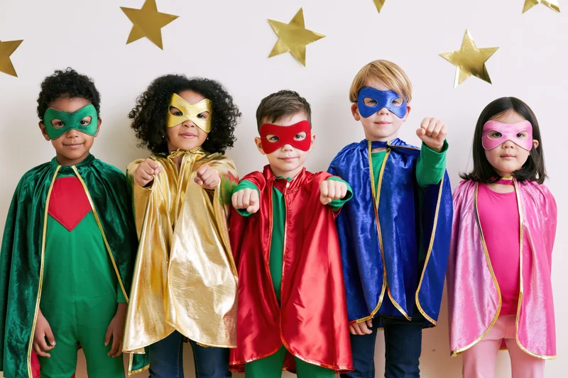 Five diverse children in colorful superhero costumes posing together indoors
