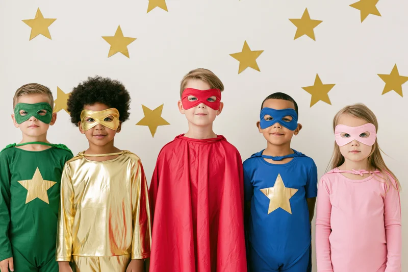 Five children in colorful superhero costumes posing together indoors