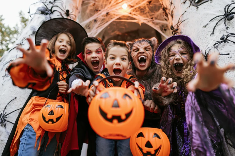 Children in halloween costumes posing with pumpkin buckets at a decorated doorway