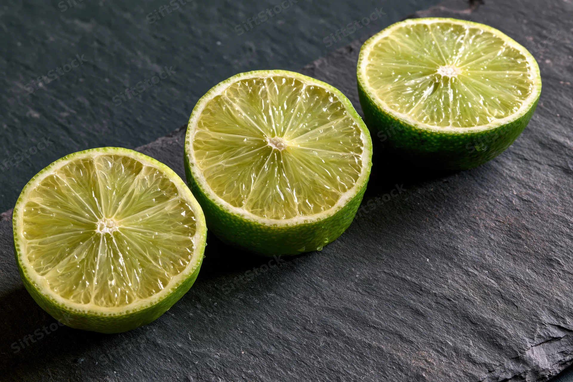 Three lime halves cut-side up arranged in a diagonal row on a dark slate surface