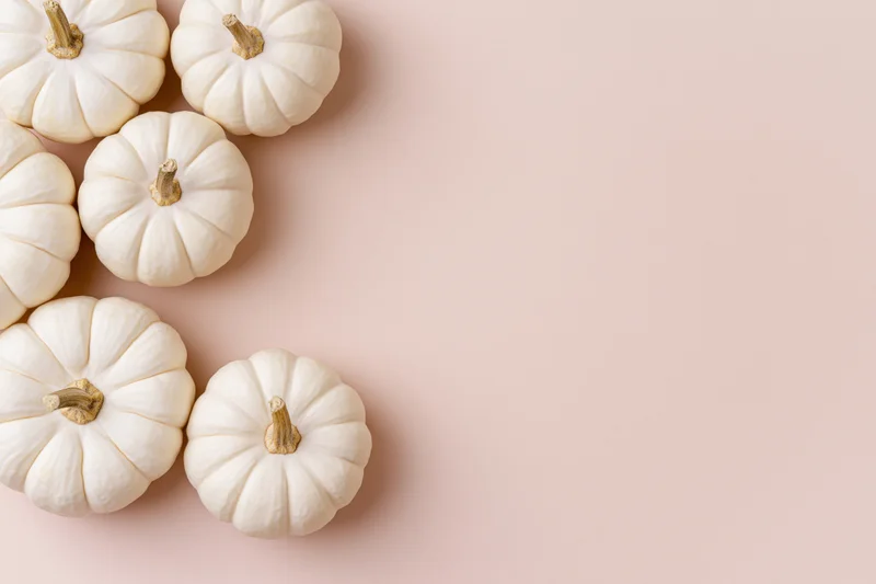 White baby boo pumpkins arranged in a corner on a soft beige surface with copyspace