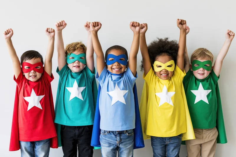 Five children in superhero costumes with raised fists standing in a row