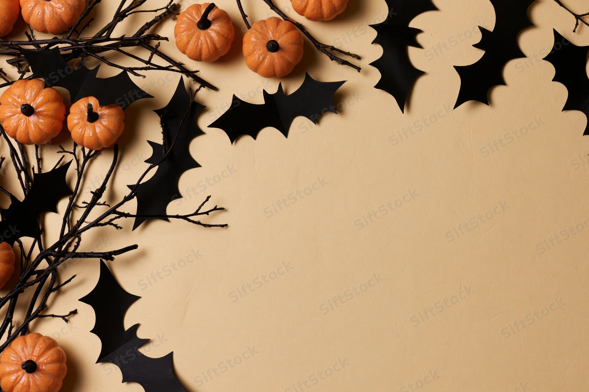 Halloween decoration arrangement with small orange pumpkins, black paper bats, and branches on beige surface