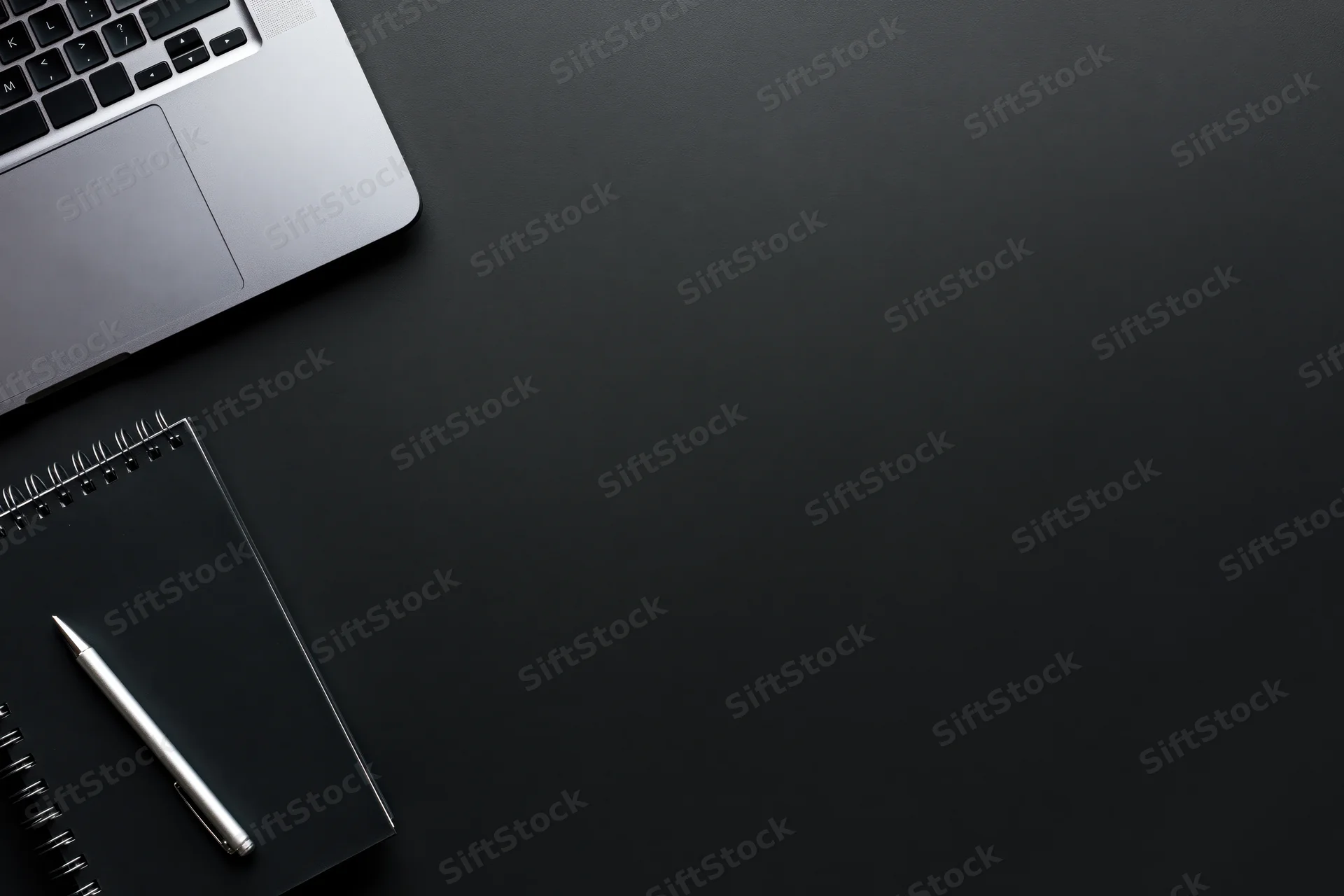 Silver laptop and notebook with pen on black desk surface