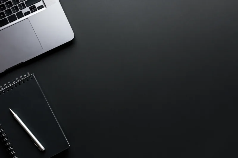 Silver laptop and notebook with pen on black desk surface