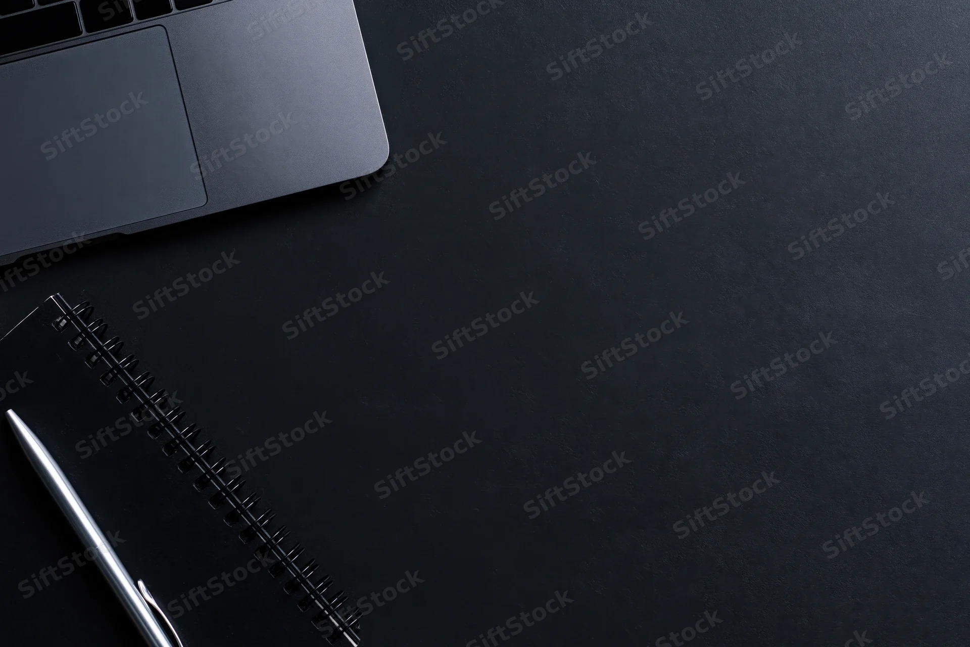 Silver laptop and notebook with pen on black desk surface, top view