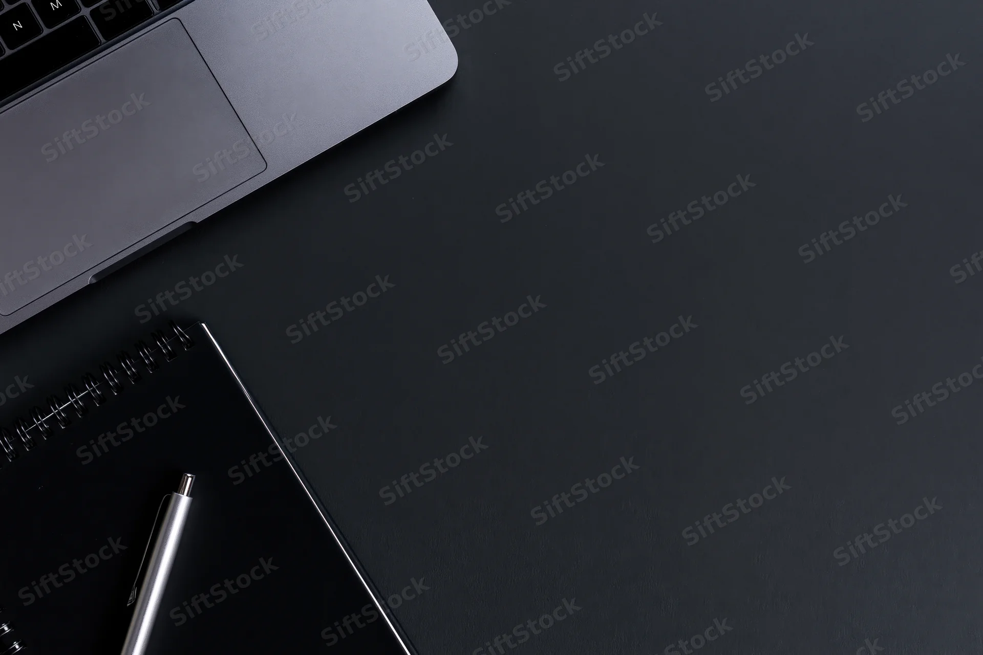 Silver laptop and notebook with pen on dark desk surface