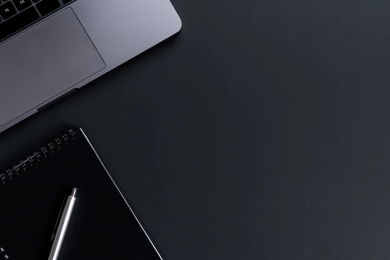 Silver laptop and notebook with pen on dark desk surface