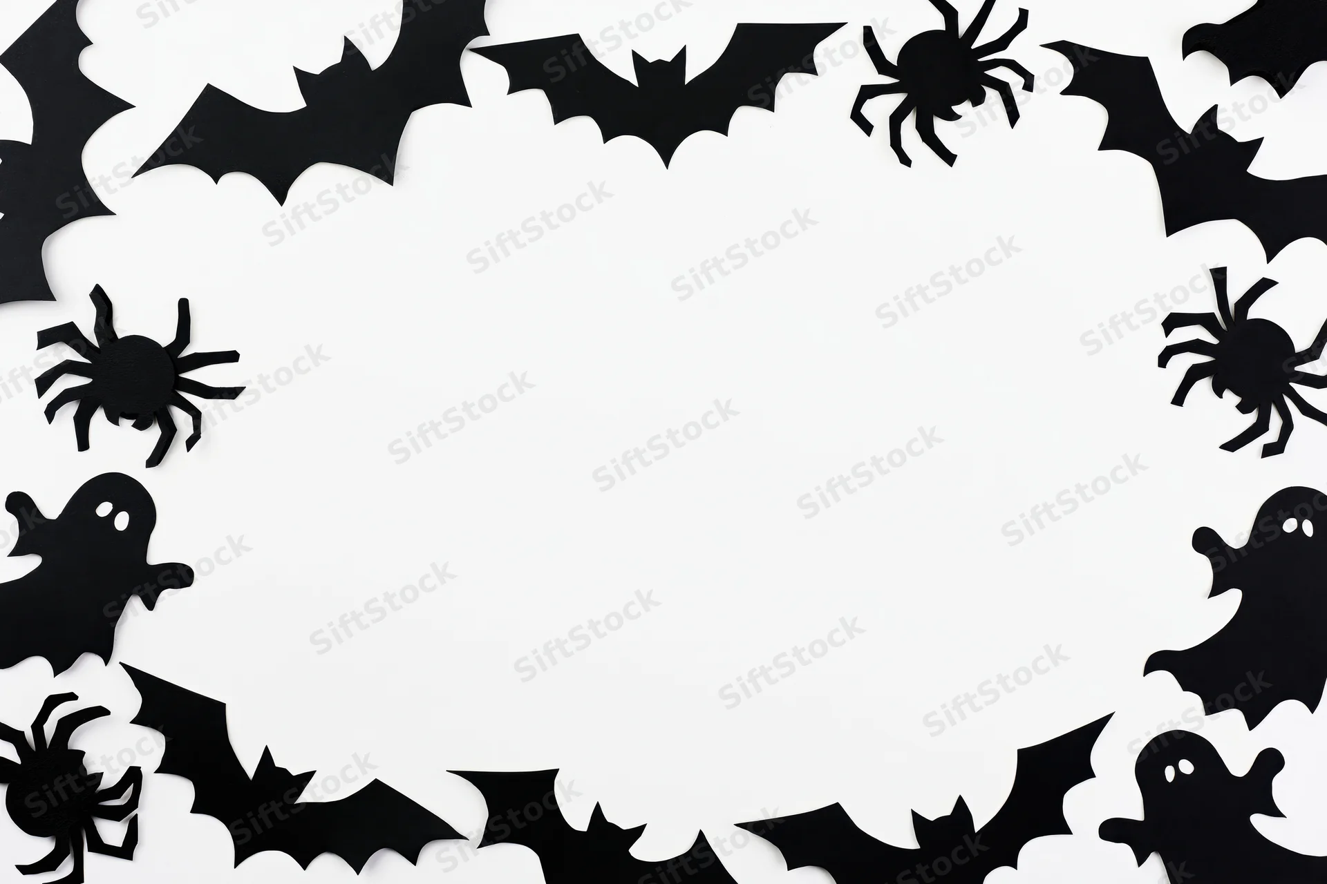 Black paper halloween cutouts of bats spiders and ghosts arranged in a circular frame on white background
