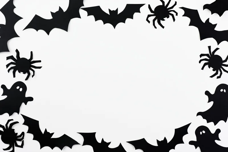 Black paper halloween cutouts of bats spiders and ghosts arranged in a circular frame on white background