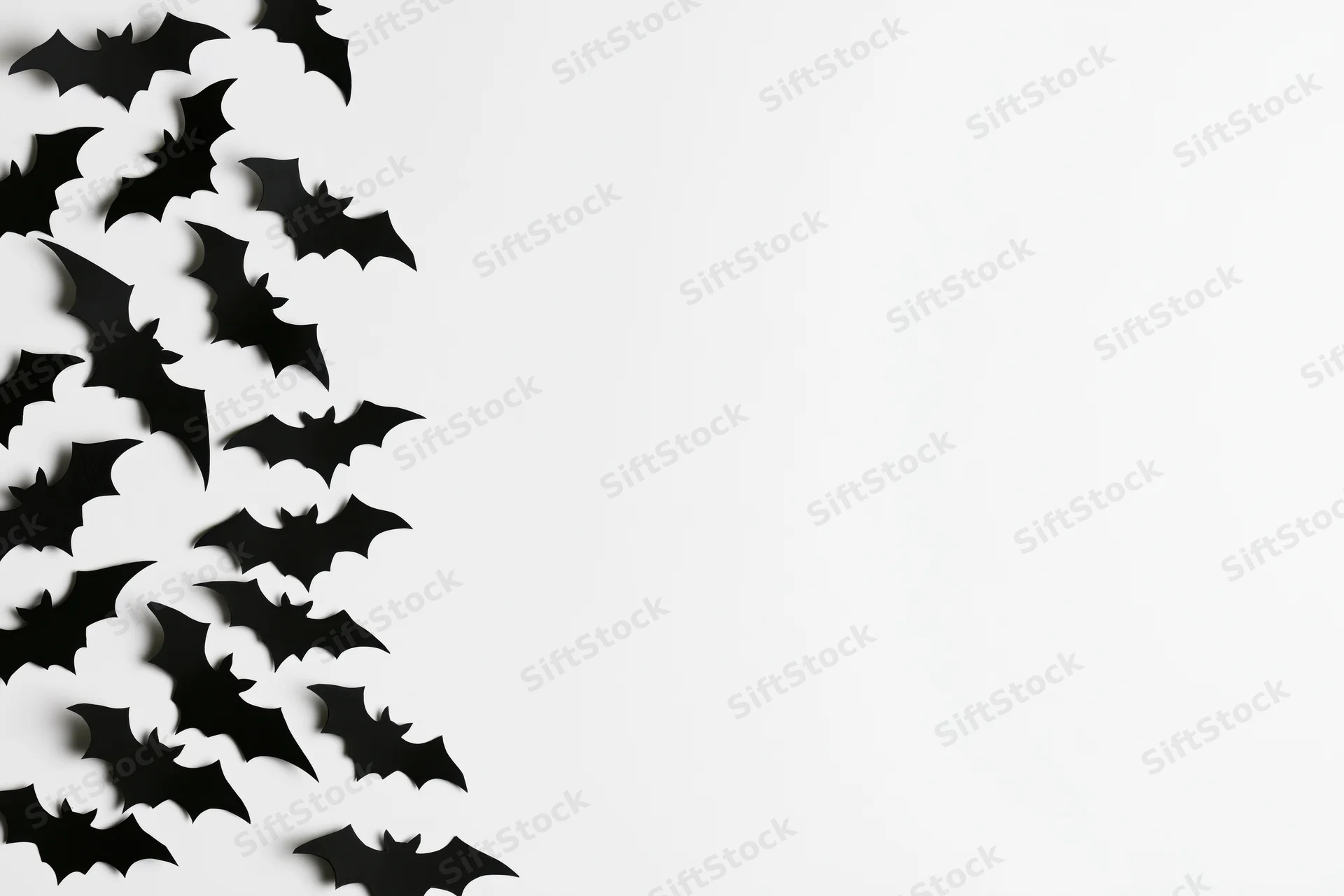 Black paper bat cutouts scattered in a flat lay on white background with copyspace