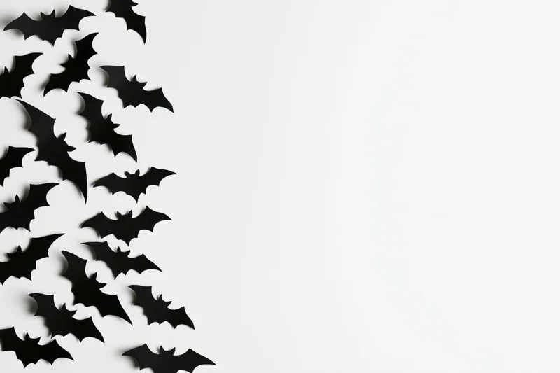 Black paper bat cutouts scattered in a flat lay on white background with copyspace