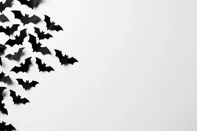 Black paper bat cutouts scattered on white surface for halloween decoration