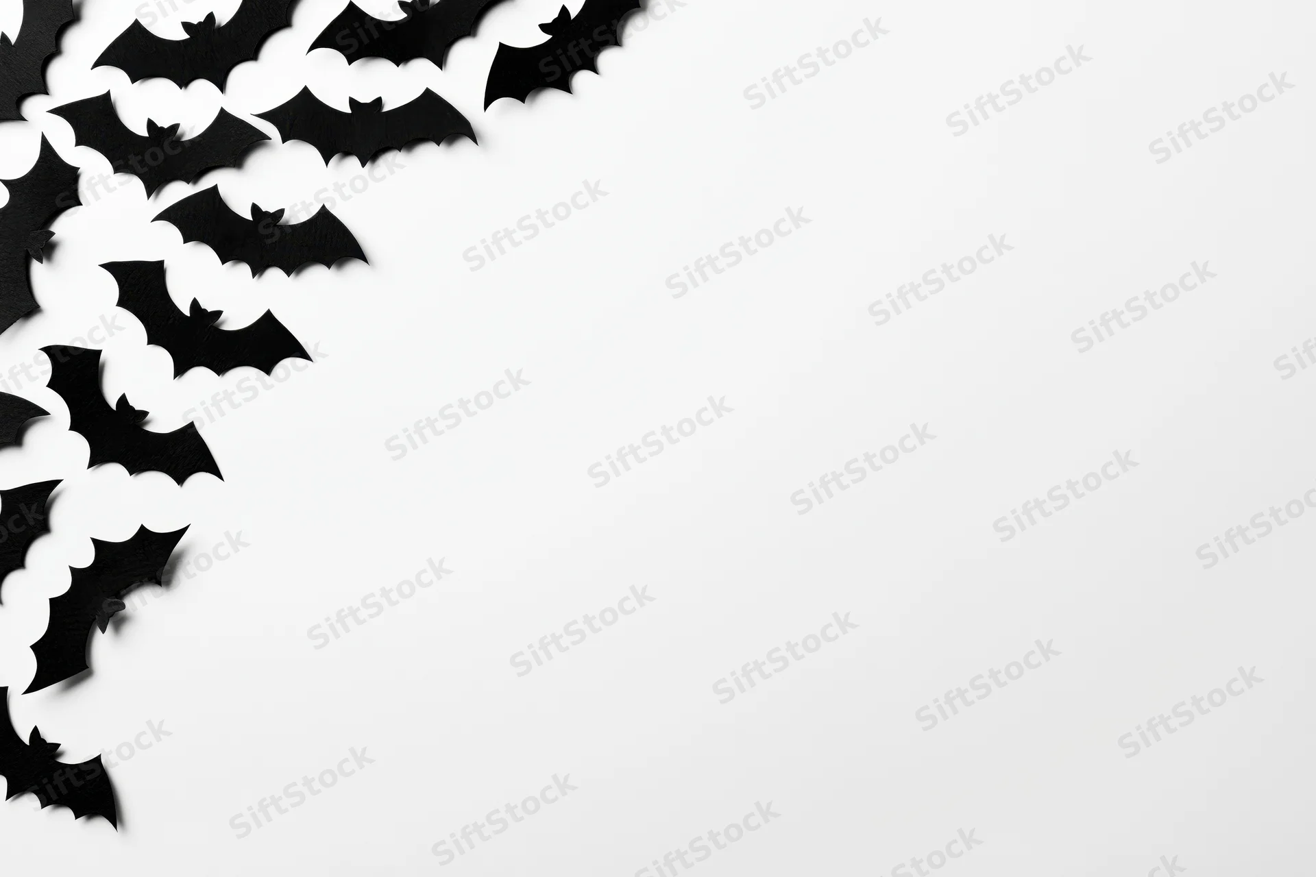 Black paper bat cutouts arranged in scattered pattern on white surface with copyspace