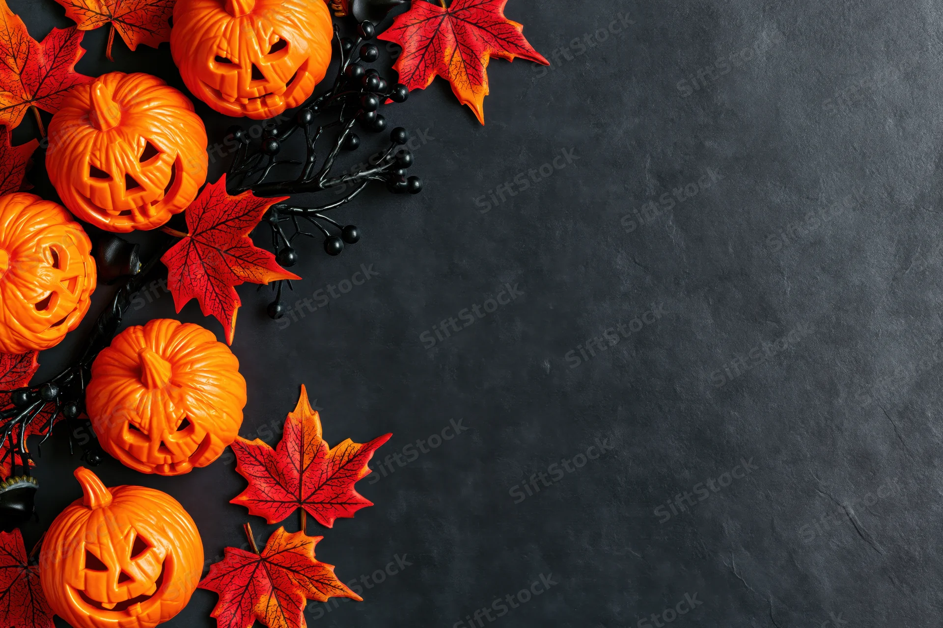 Carved jack-o-lanterns and red maple leaves arranged in corner on dark surface with copyspace
