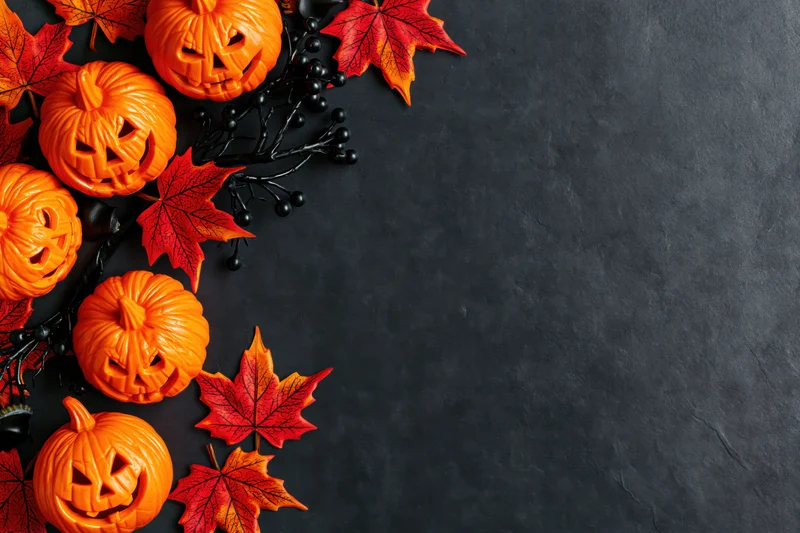 Carved jack-o-lanterns and red maple leaves arranged in corner on dark surface with copyspace