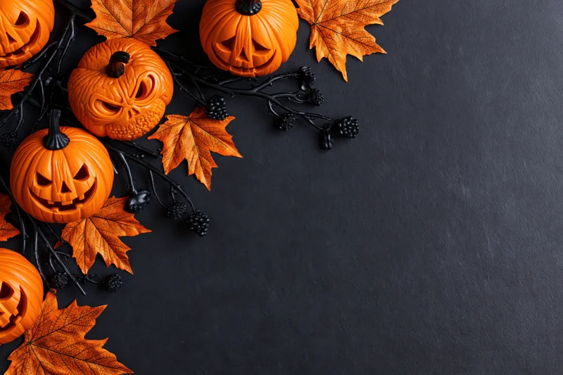 Carved jack-o-lanterns and autumn leaves arranged on dark surface with copyspace