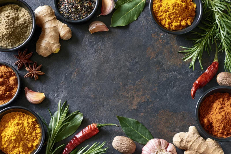 Cooking spices and herbs arranged in a circular flat lay on dark textured surface with central copyspace