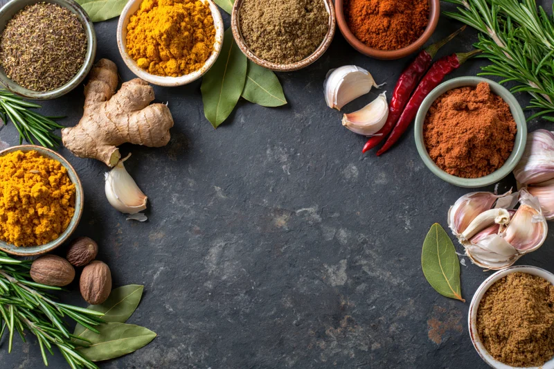 Cooking spices and herbs arranged around the edge of a dark stone surface