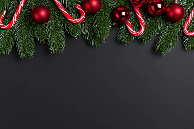 Pine branches with red ornaments and candy canes arranged along top edge on dark background