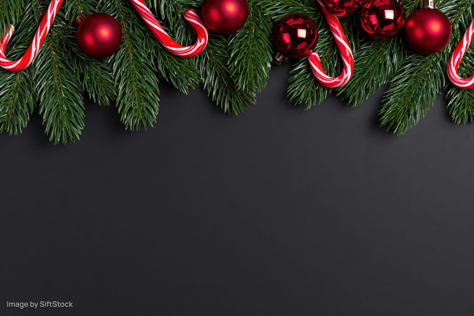Pine branches with red ornaments and candy canes arranged along top edge on dark background