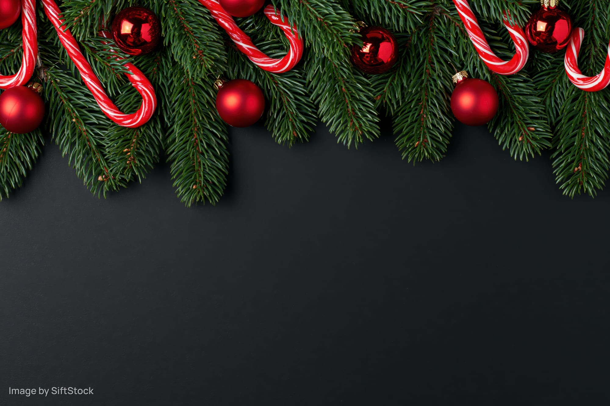 Pine branches with red ornaments and candy canes arranged along top edge of black surface