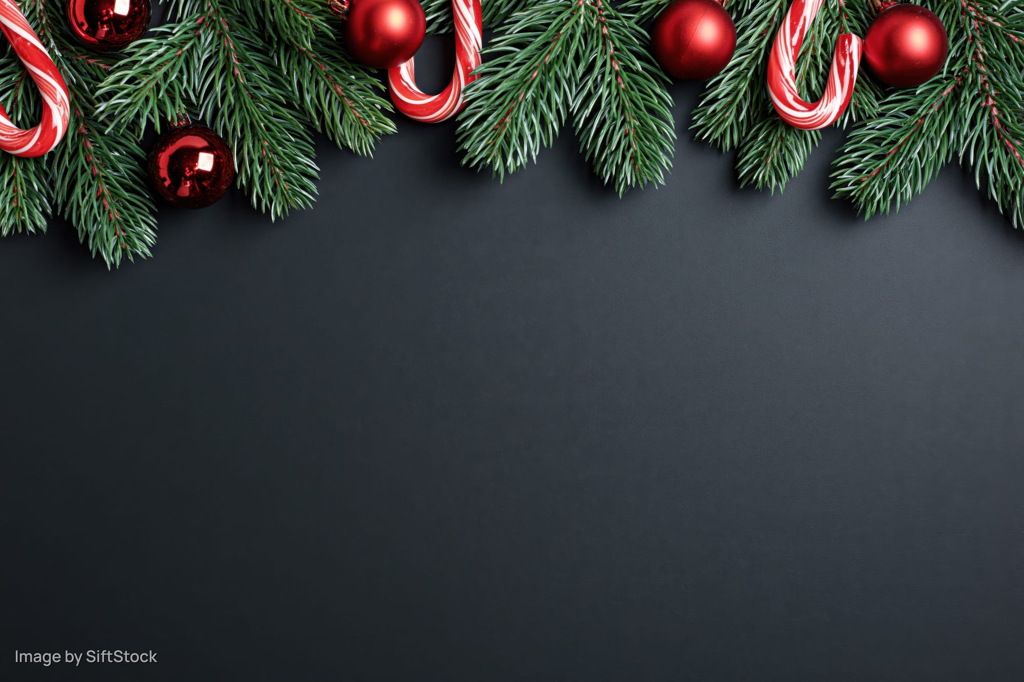 Pine branches with red ornaments and candy canes arranged along top edge of dark surface