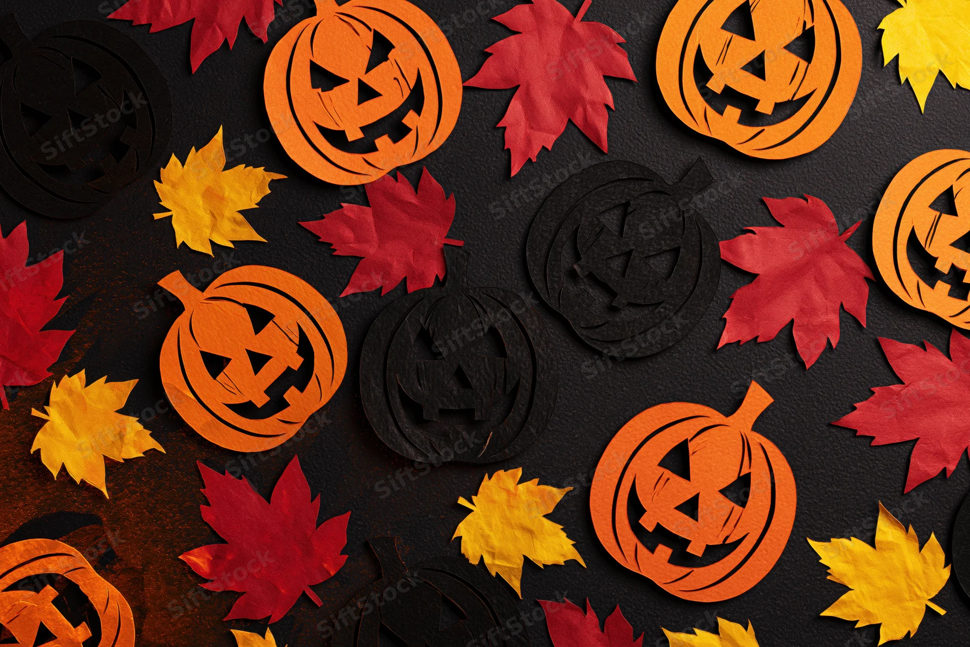 Handmade paper jack-o-lanterns and autumn leaves arranged in a flat lay on dark surface