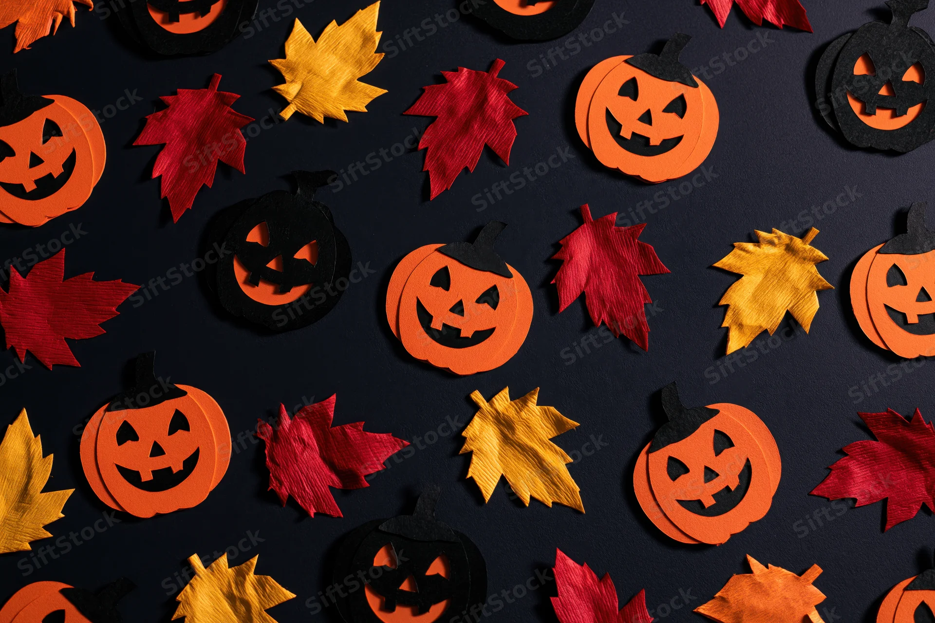 Handmade paper jack-o-lanterns and autumn leaves arranged in a flat lay on dark surface